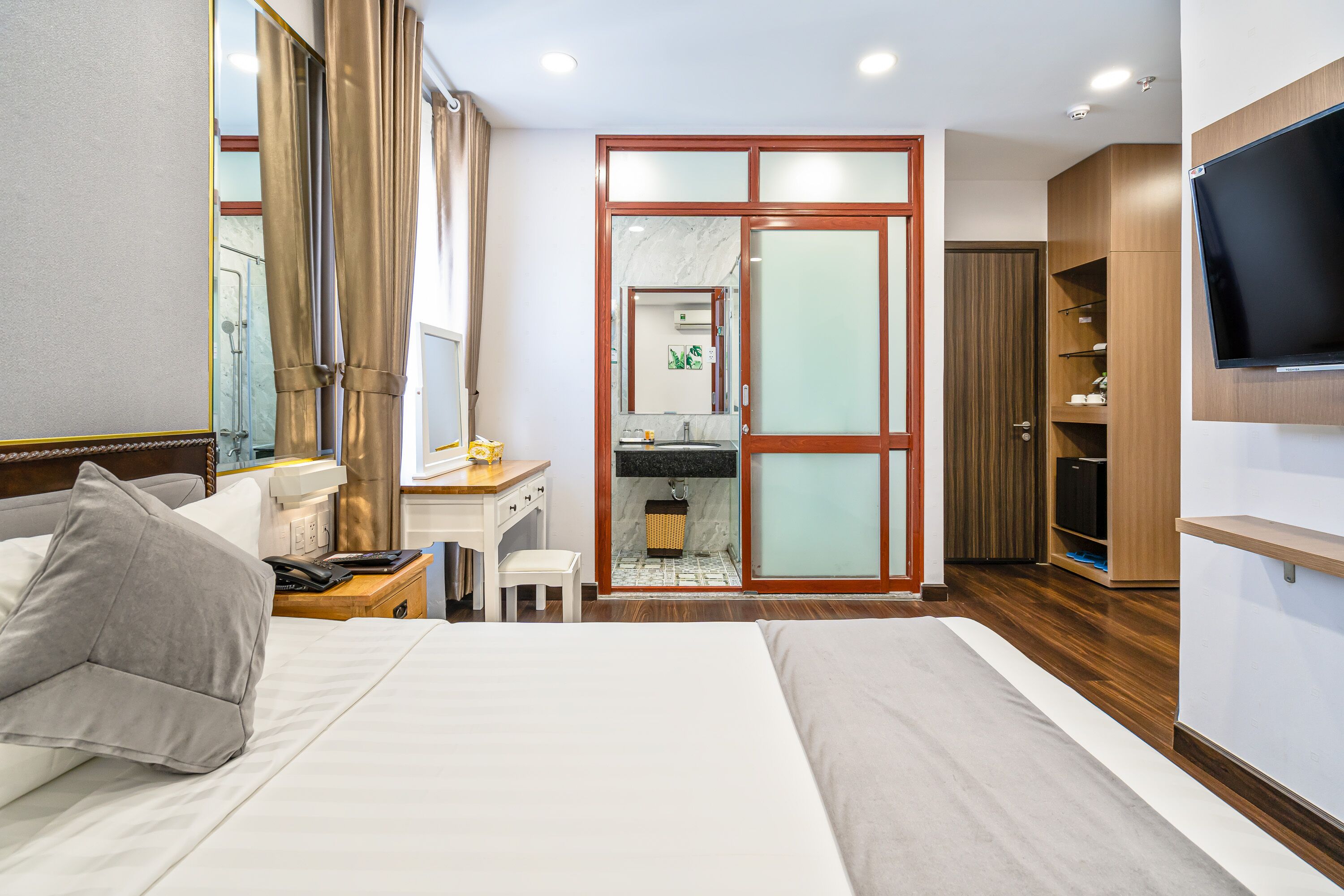 Une chambre d’hôtel comprenant un grand lit, un bureau avec une chaise, une coiffeuse avec un miroir, un téléviseur fixé au mur et une armoire.