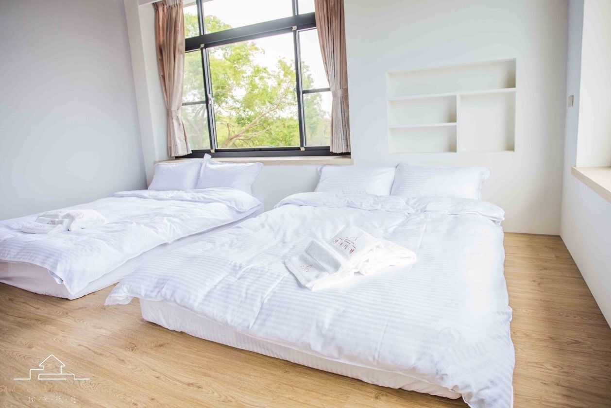 A bedroom with two beds, a window with curtains, and a built-in shelf.
