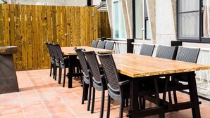 A row of wooden tables and chairs in an outdoor patio area with a wooden fence and tiled flooring. - shih.kuang (Tainan)