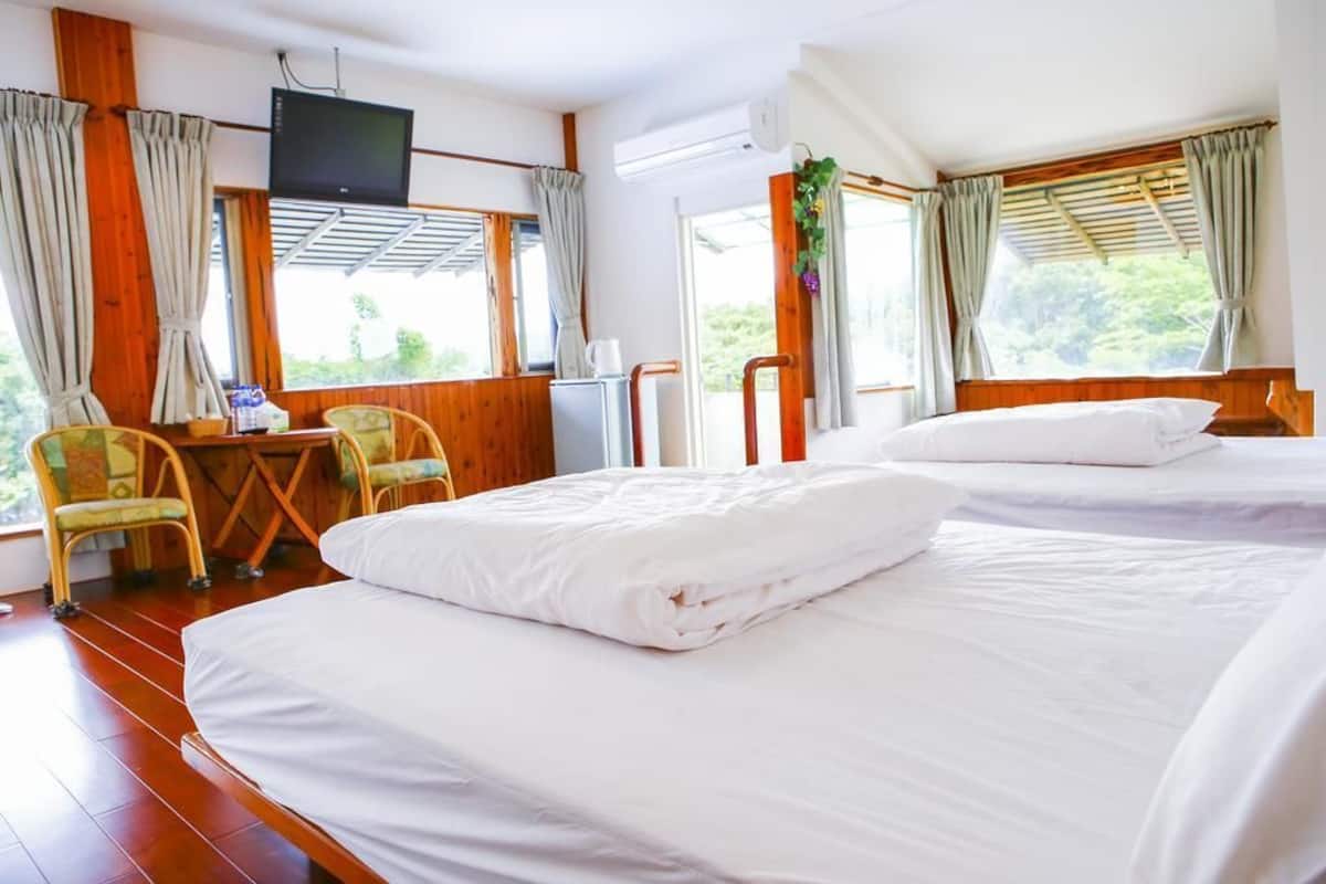 Habitació d'hotel amb dos llits, televisió, escriptori amb cadira i grans finestres amb cortines.