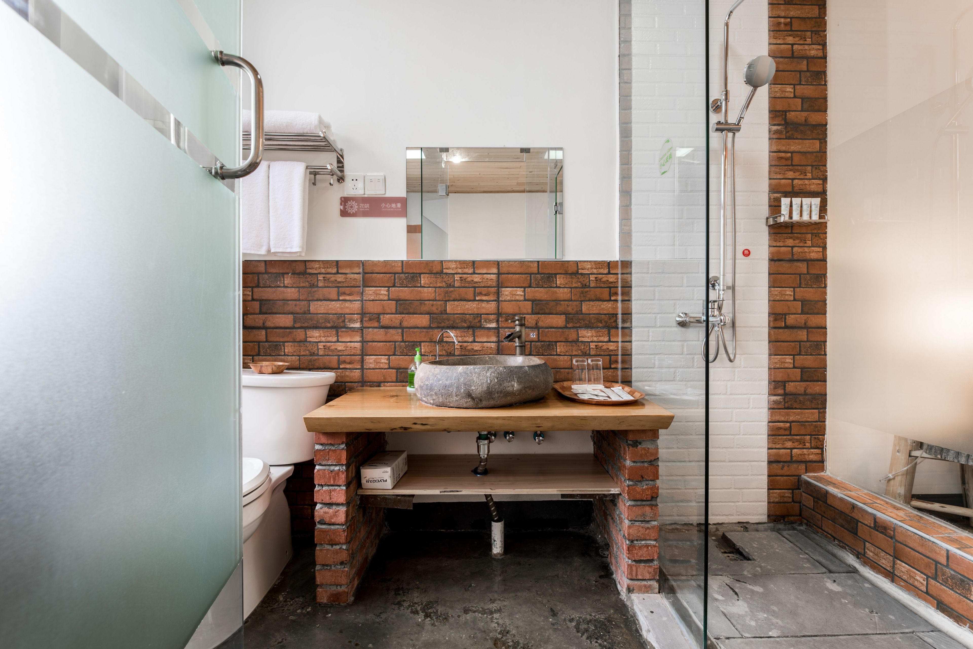 A bathroom with a stone sink, a mirror, a shower, and a toilet.