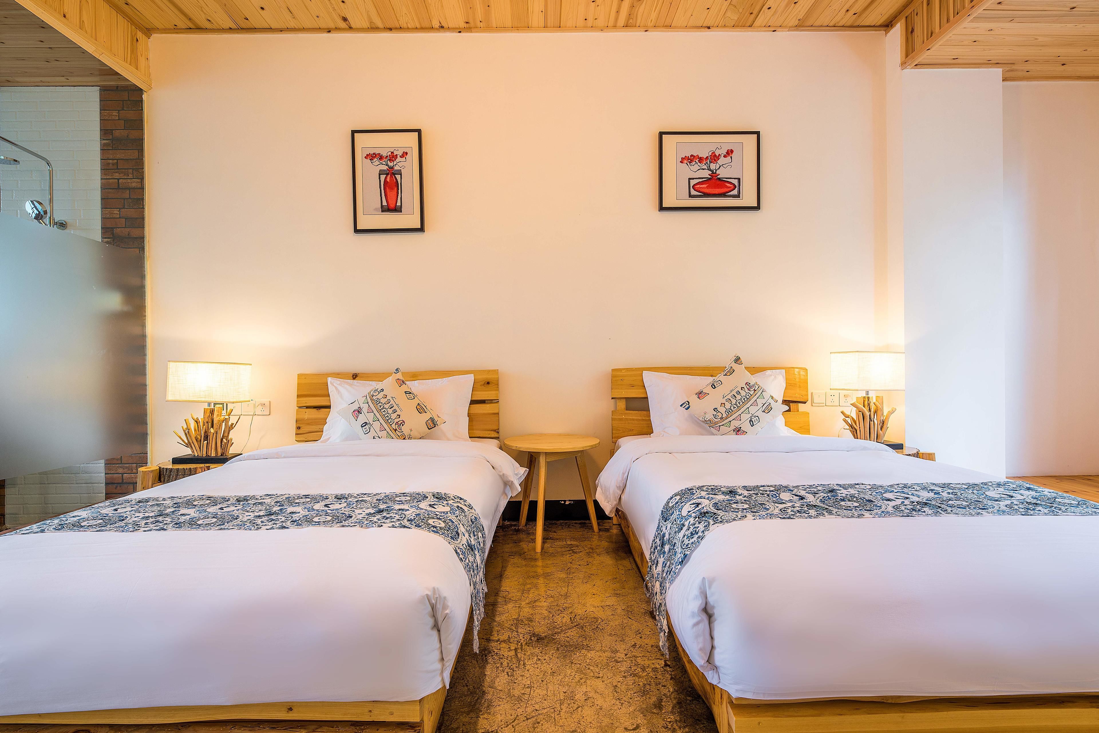A hotel room with two beds, a small wooden table, and two wall-mounted lamps.