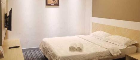 A hotel room with a bed, a desk, a chair, a trash bin, and a wall-mounted TV.