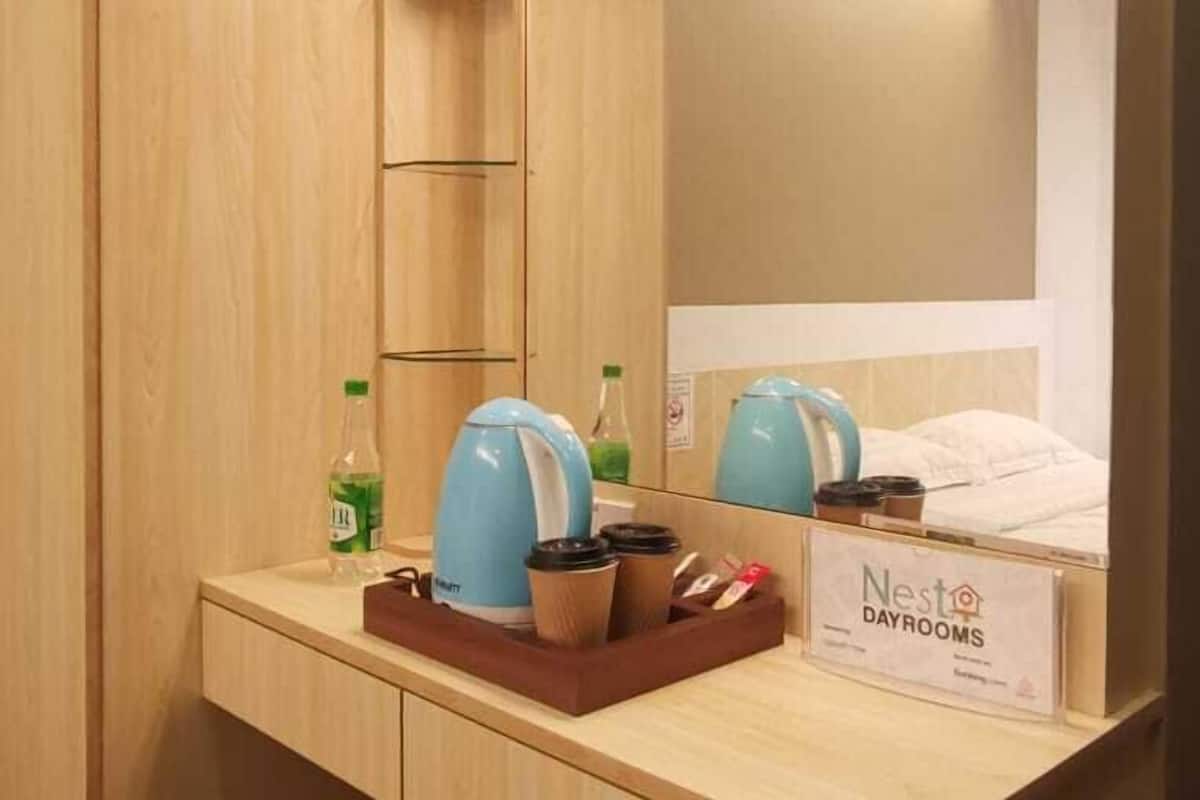 Ein Hotelzimmer mit einem hölzernen Schminktisch, einem Spiegel, einer kleinen Ablage mit einer Vase, einer Kaffeemaschine und einem Schild für Nest Dayrooms.