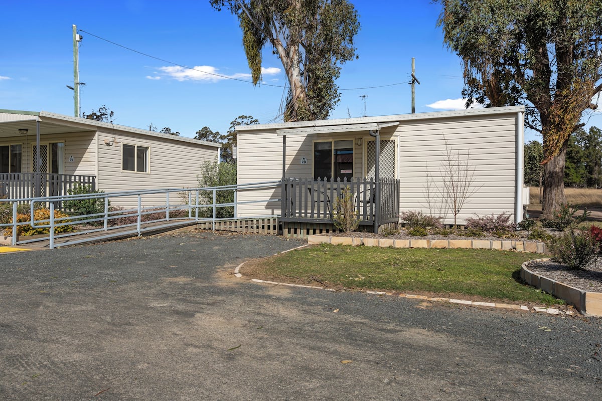 A row of mobile homes with a paved driveway and a small grassy area with a fence.