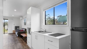 A modern kitchen with white cabinetry, a built-in sink, and a window with a view of greenery. - Crows Nest Tourist Park (Crows Nest)