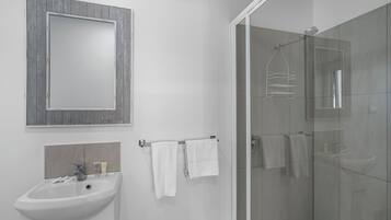 Un baño moderno con lavamanos blanco, espejo y cabina de ducha de vidrio.