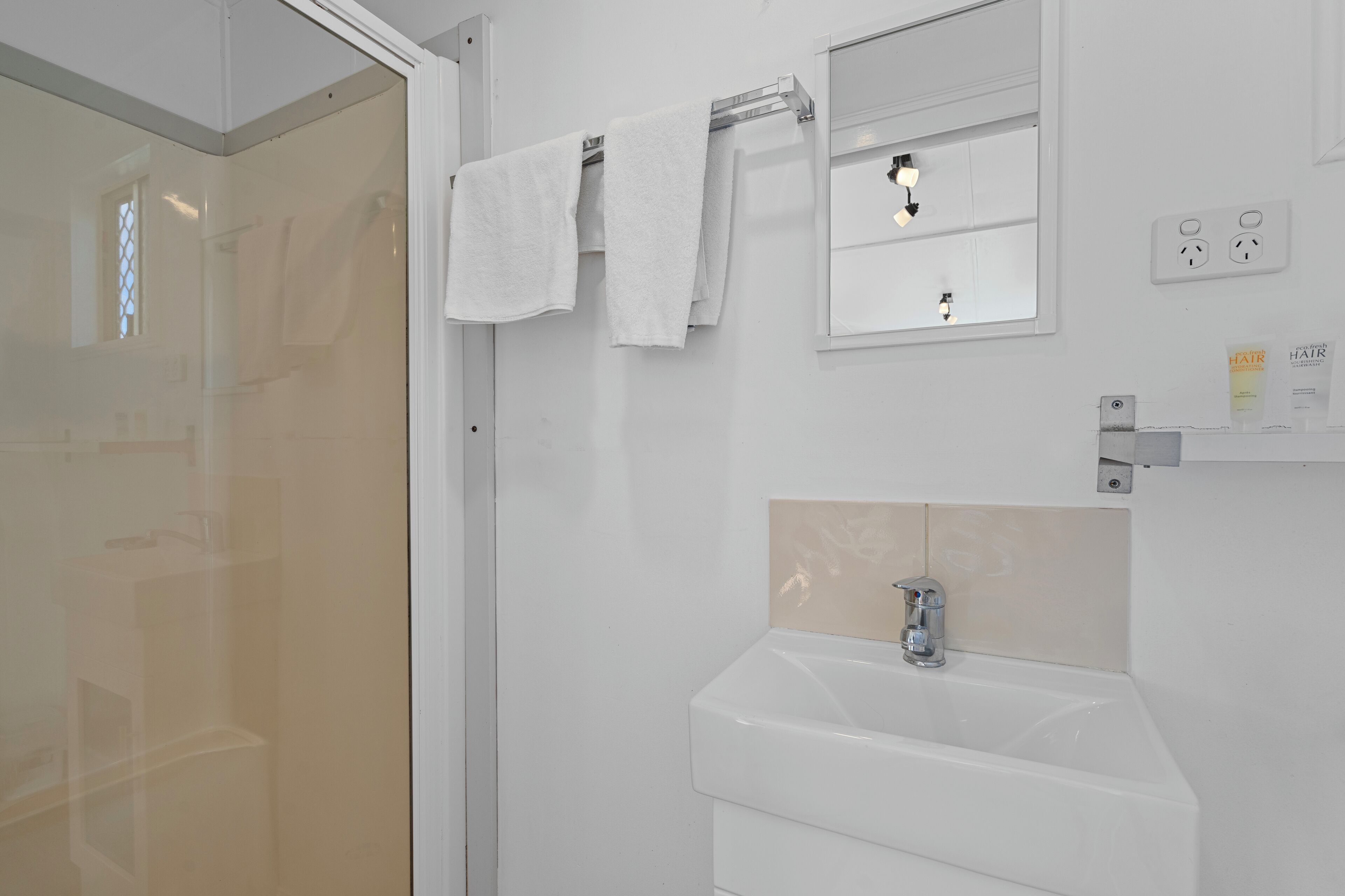 A bathroom with a white sink, a mirror, and two towels hanging on a rack.