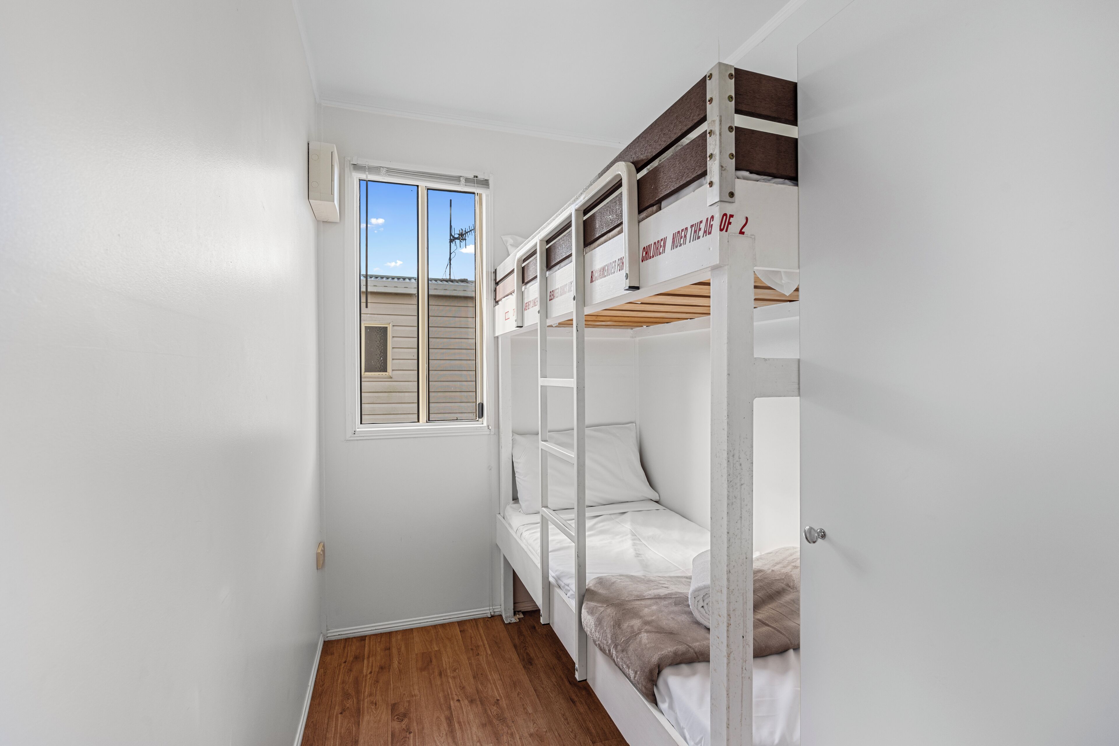 A small, white-walled room with a bunk bed, a window, and a door.