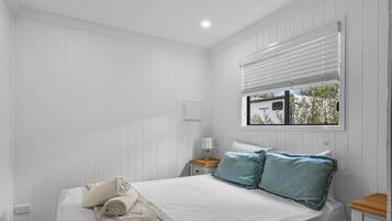 A bedroom with a bed, a nightstand, a window with blinds, and a view of the outside.