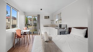 A modern hotel room with a bed, a desk with a chair, a kitchenette, and a view of the outside. - Crows Nest Tourist Park (Crows Nest)