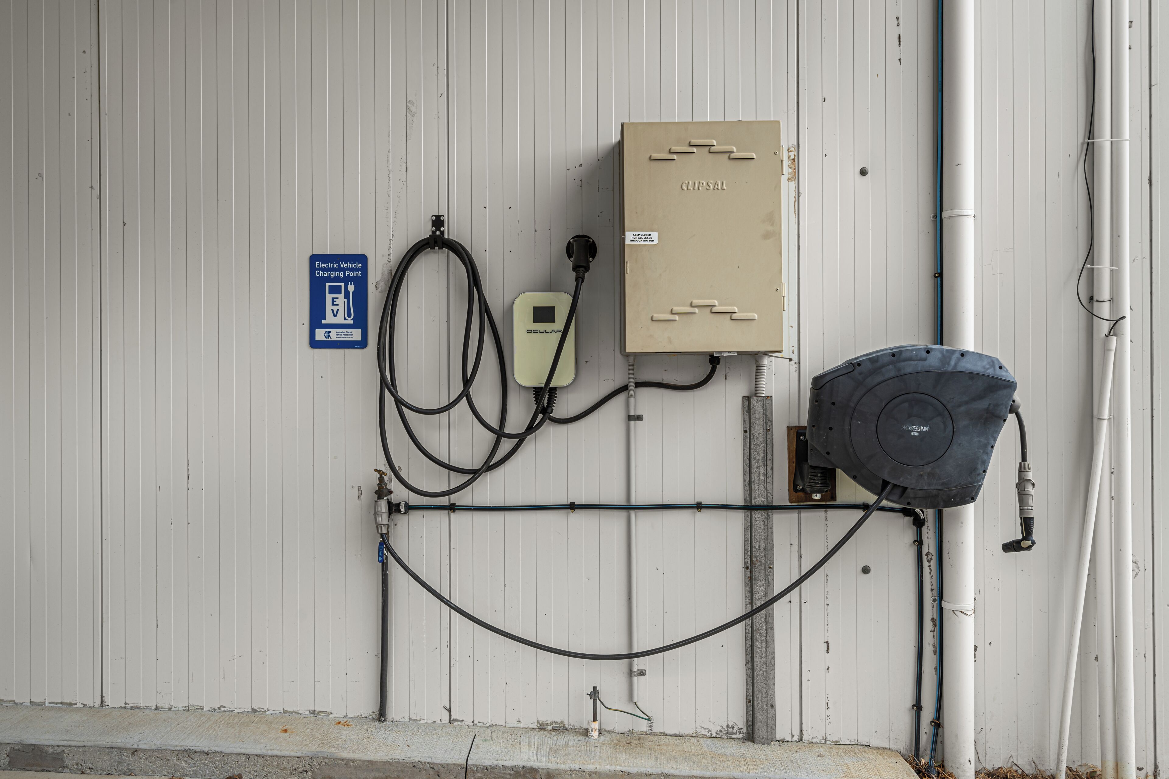 Een technische ruimte met een oplaadpunt voor elektrische voertuigen, een bedieningspaneel en een waterpomp.