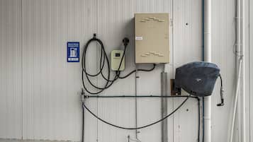 Een technische ruimte met een oplaadpunt voor elektrische voertuigen, een bedieningspaneel en een waterpomp.
