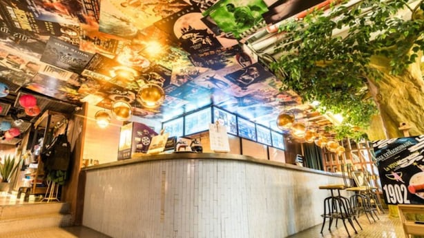 Un espace bar avec un comptoir, des luminaires suspendus et un plafond décoré d’une fresque murale.
