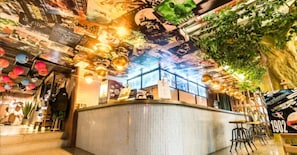 Una zona de bar con barra, luces colgantes y un techo cubierto de murales.