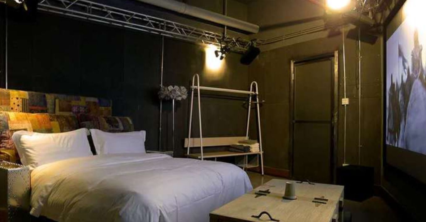Een hotelkamer met een stapelbed, een kleine tafel met een kopje, een projecter en een poster aan de muur.
