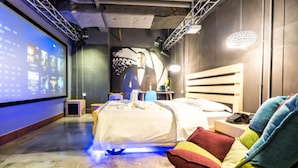 Une chambre d’hôtel équipée d’un lit, d’un bureau, d’une chaise, d’un écran diffusant du contenu et d’un projecteur fixé au mur.