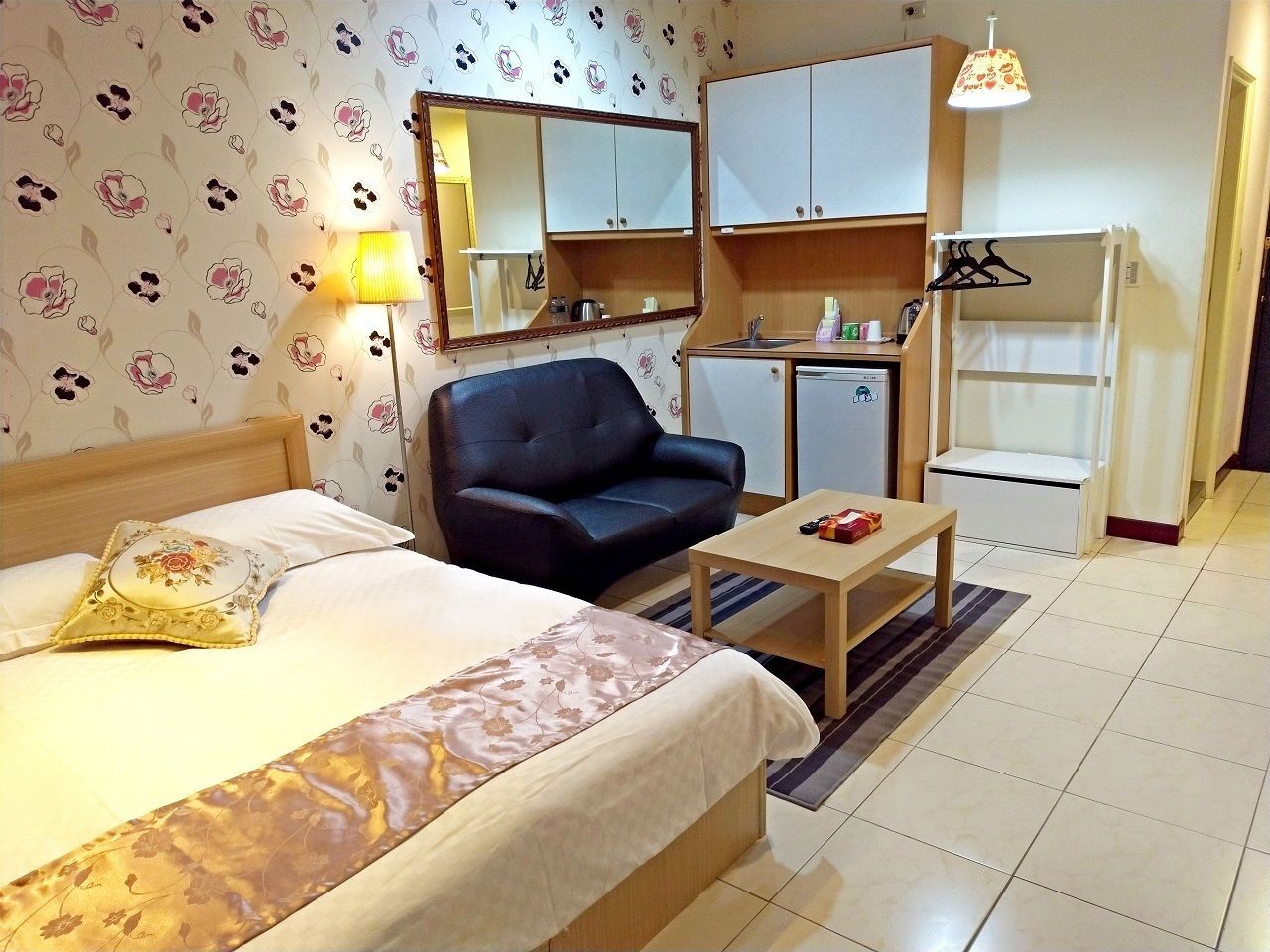 Una habitación de hotel con cama, sofá, mesita, kitchenette y espejo.
