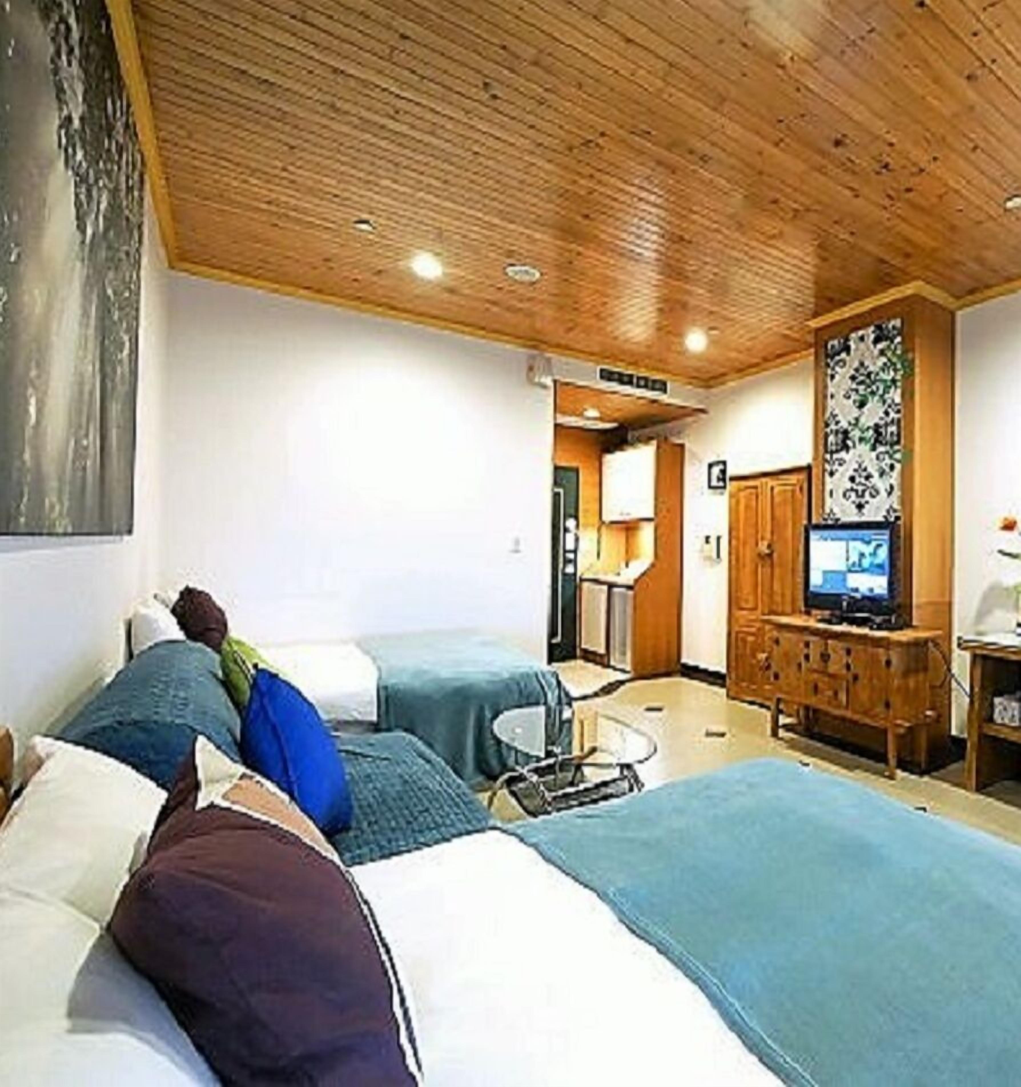 A hotel room with two beds, a wooden ceiling, a television, and a small table.