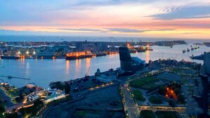 An aerial view of a coastal city at dusk with a prominent modern building, a marina, and a bridge. - 85 Prague Homestay (Kaohsiung)