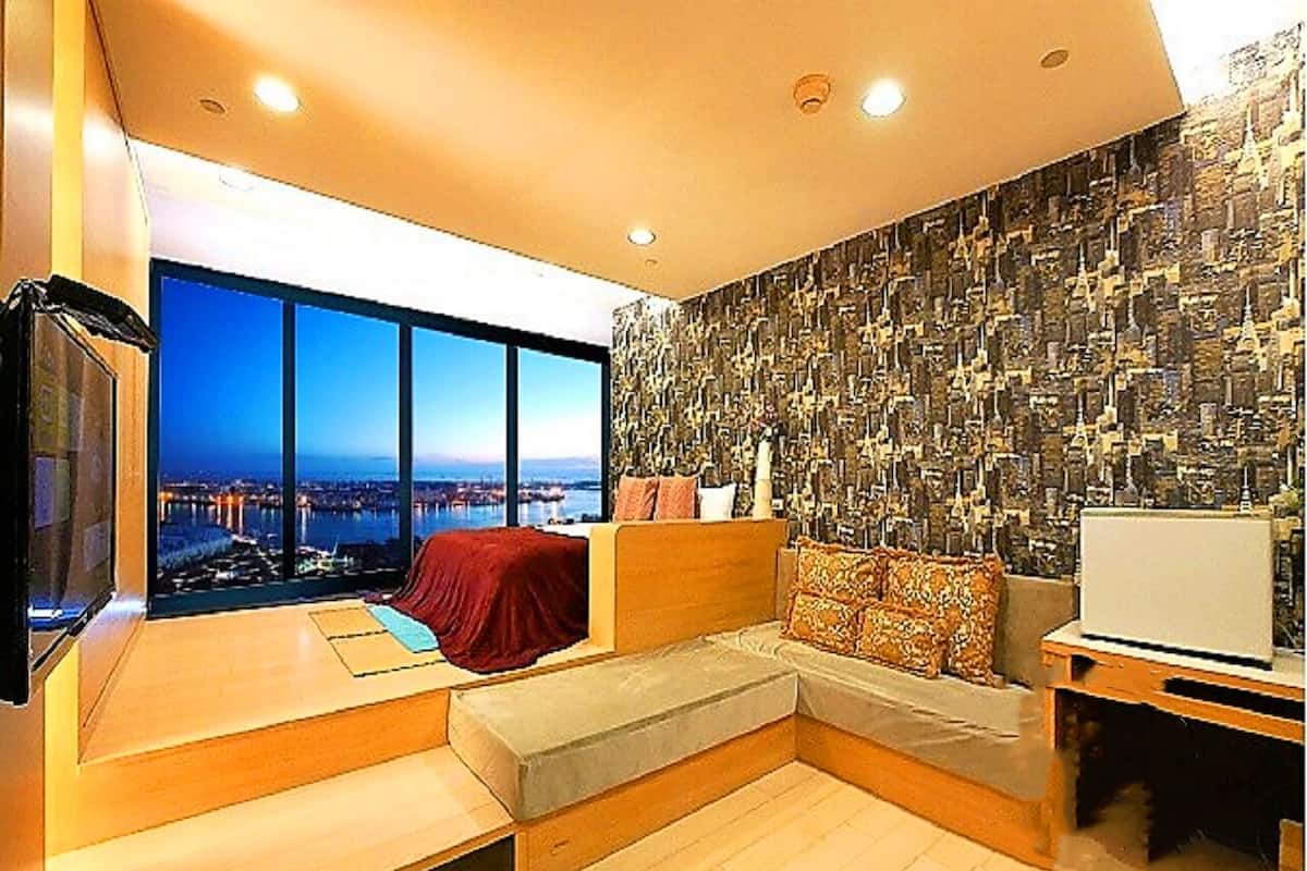 A modern living room with a large window, a sofa, a TV, and a laptop on a table.