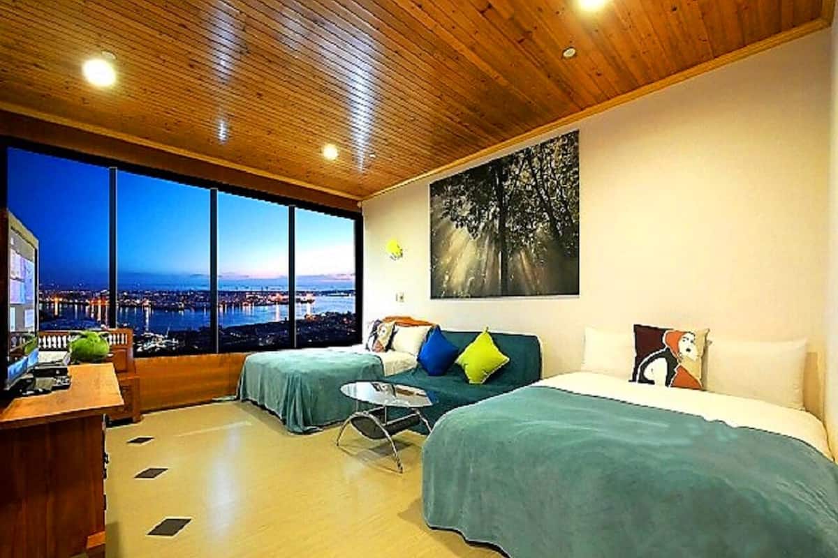 A hotel room with two beds, a desk, and a large window offering a city view.