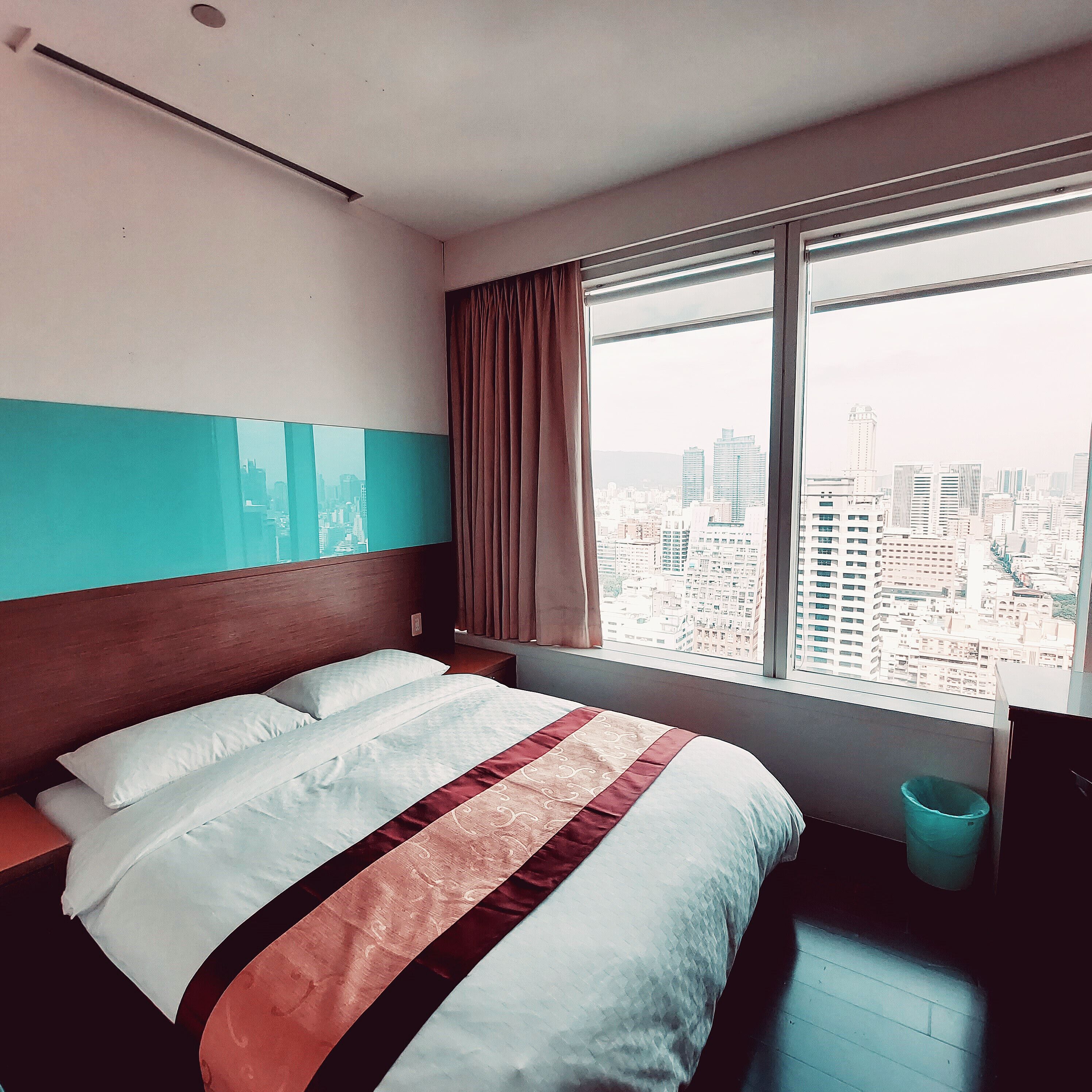 A hotel room with a large bed, a view of a cityscape, and a window with curtains.