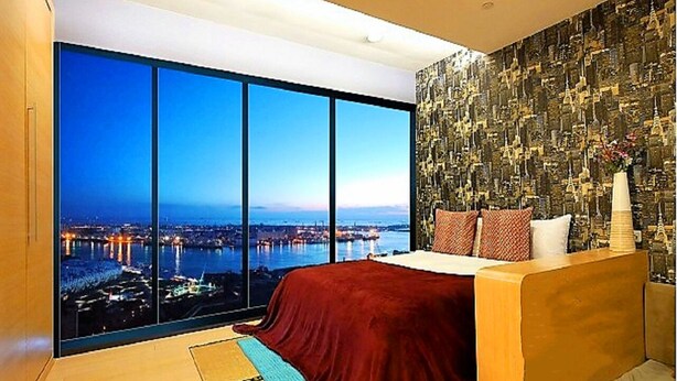 A bedroom with a large window offering a city view, a bed with a red cover, and a patterned wall. - 85 Prague Homestay (Kaohsiung)