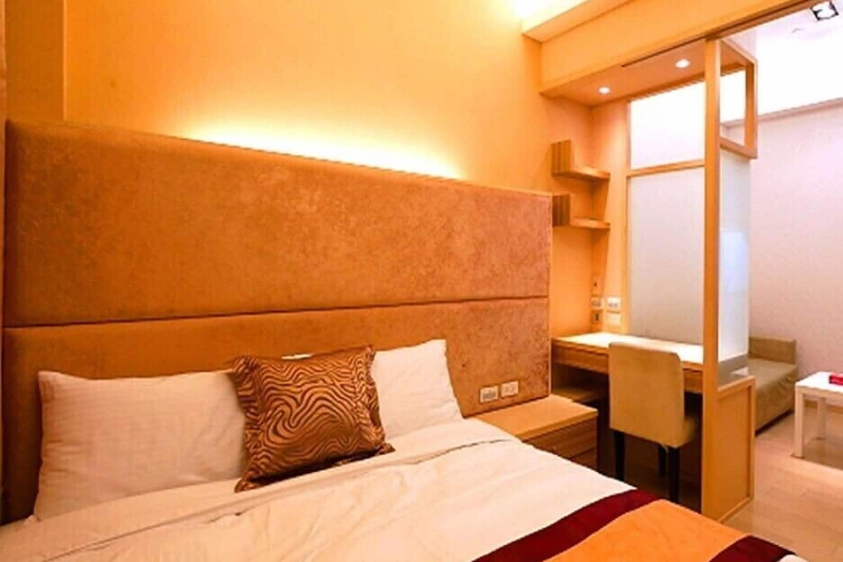 A hotel room with a large bed, a desk, and a chair.