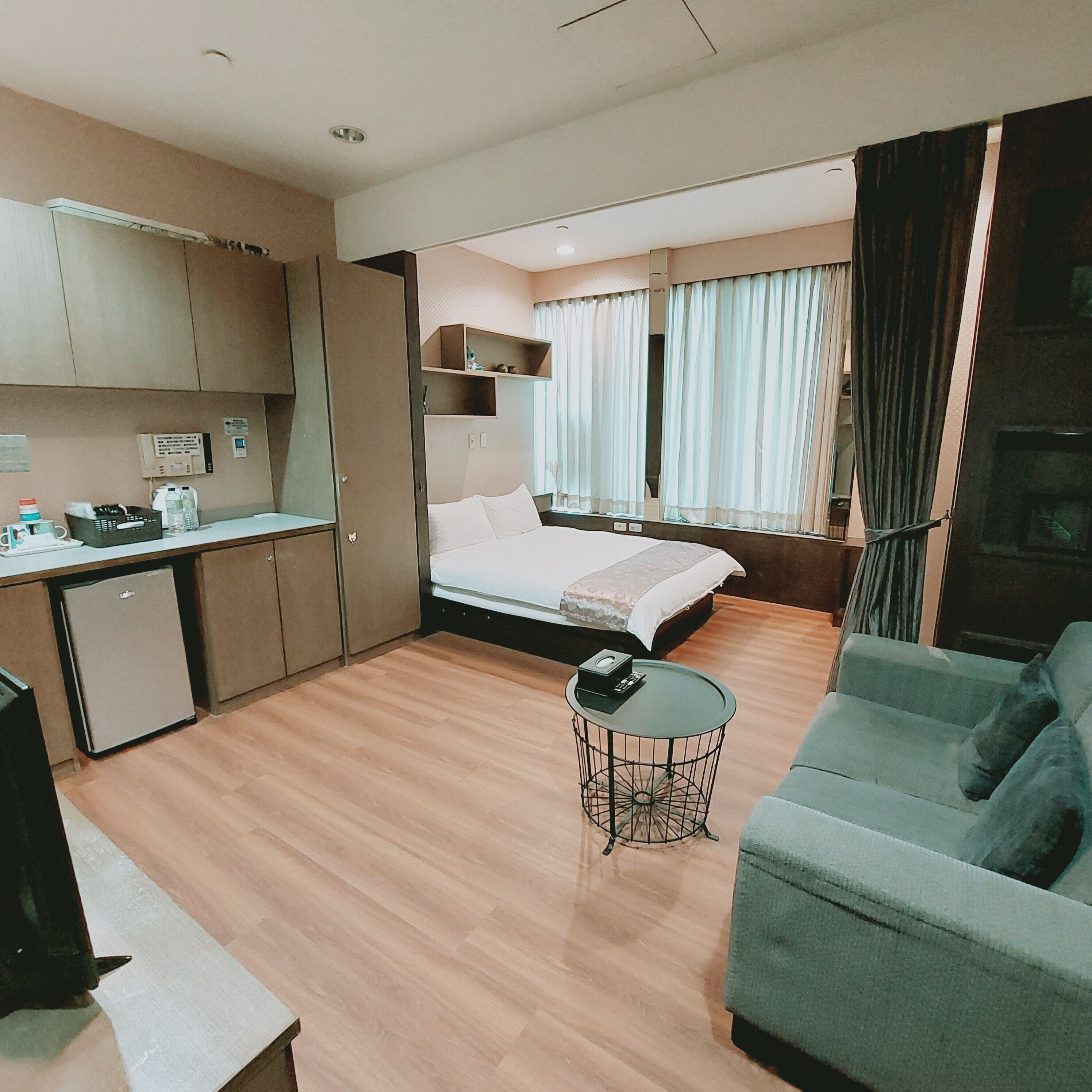 A compact hotel room with a kitchenette, a bed, a sofa, and a small table.