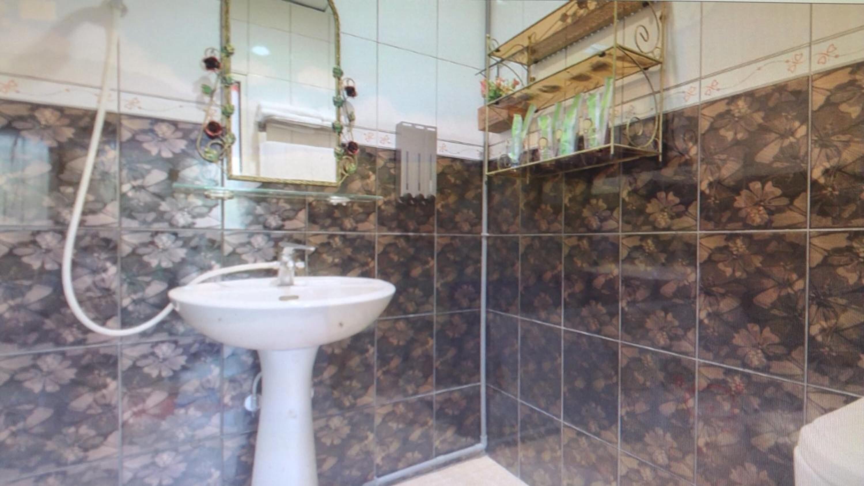 Uma casa de banho com uma pia branca, um espelho e azulejos com padrão floral.