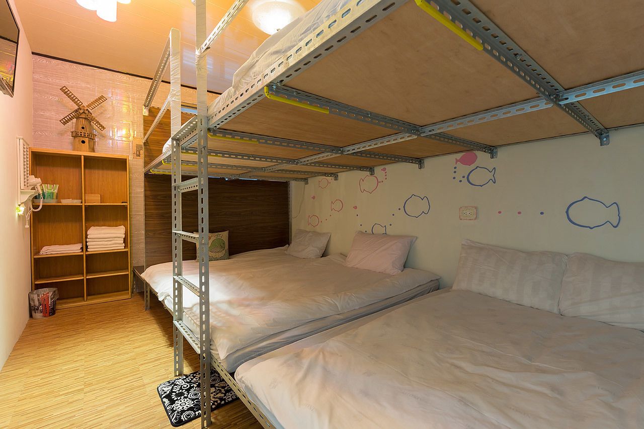 A bunk bed room with a wooden floor, metal bunk beds, a wooden shelf unit, and a windmill decoration on the wall.
