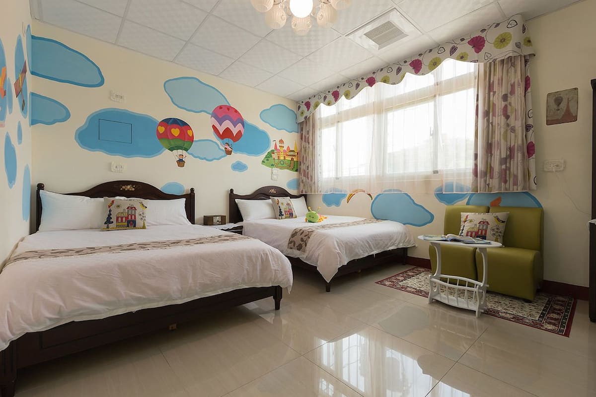 A hotel room with two beds, a green sofa, a small table, and a window with curtains.