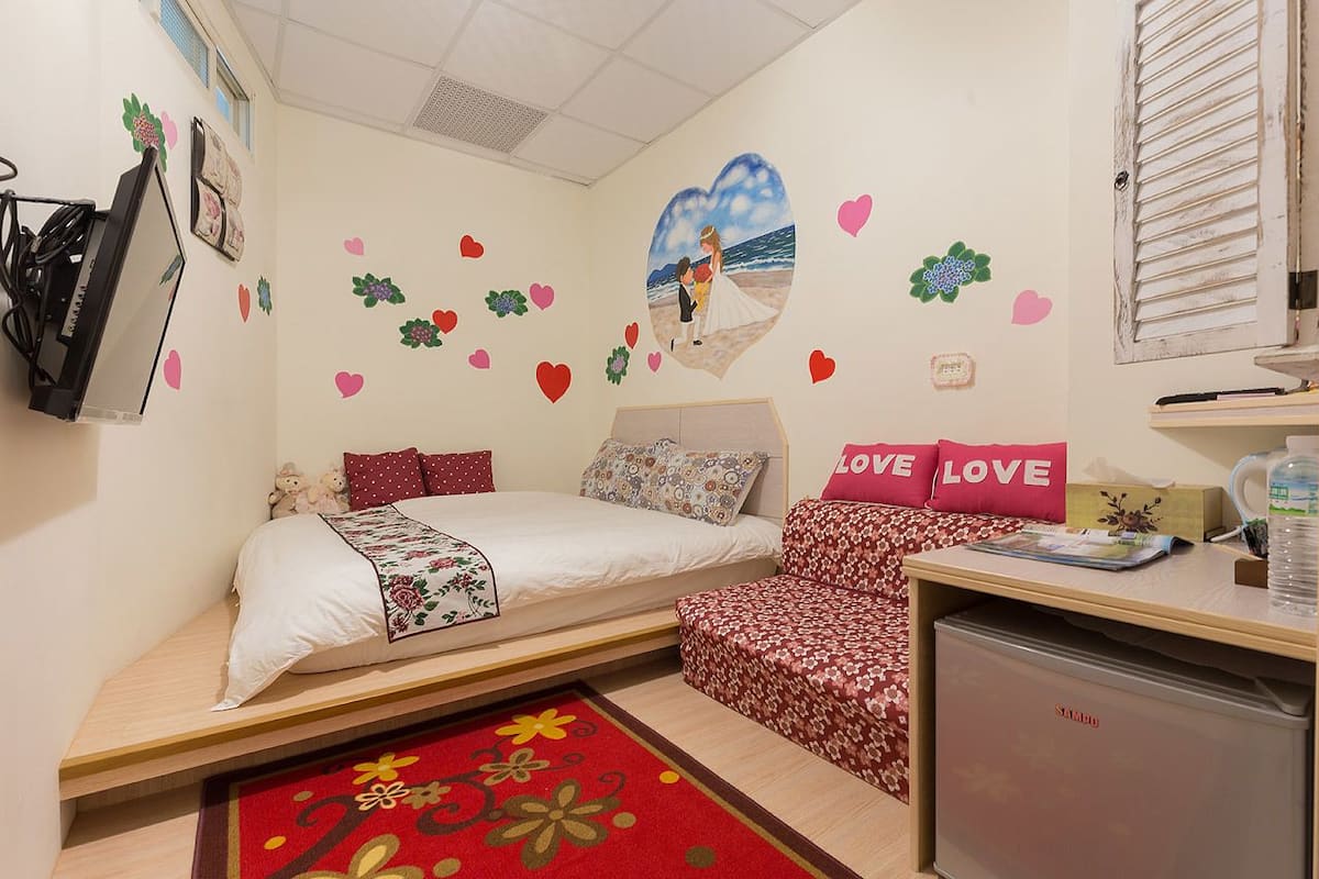 A bedroom with a bed, a desk, a chair, and a small fridge.