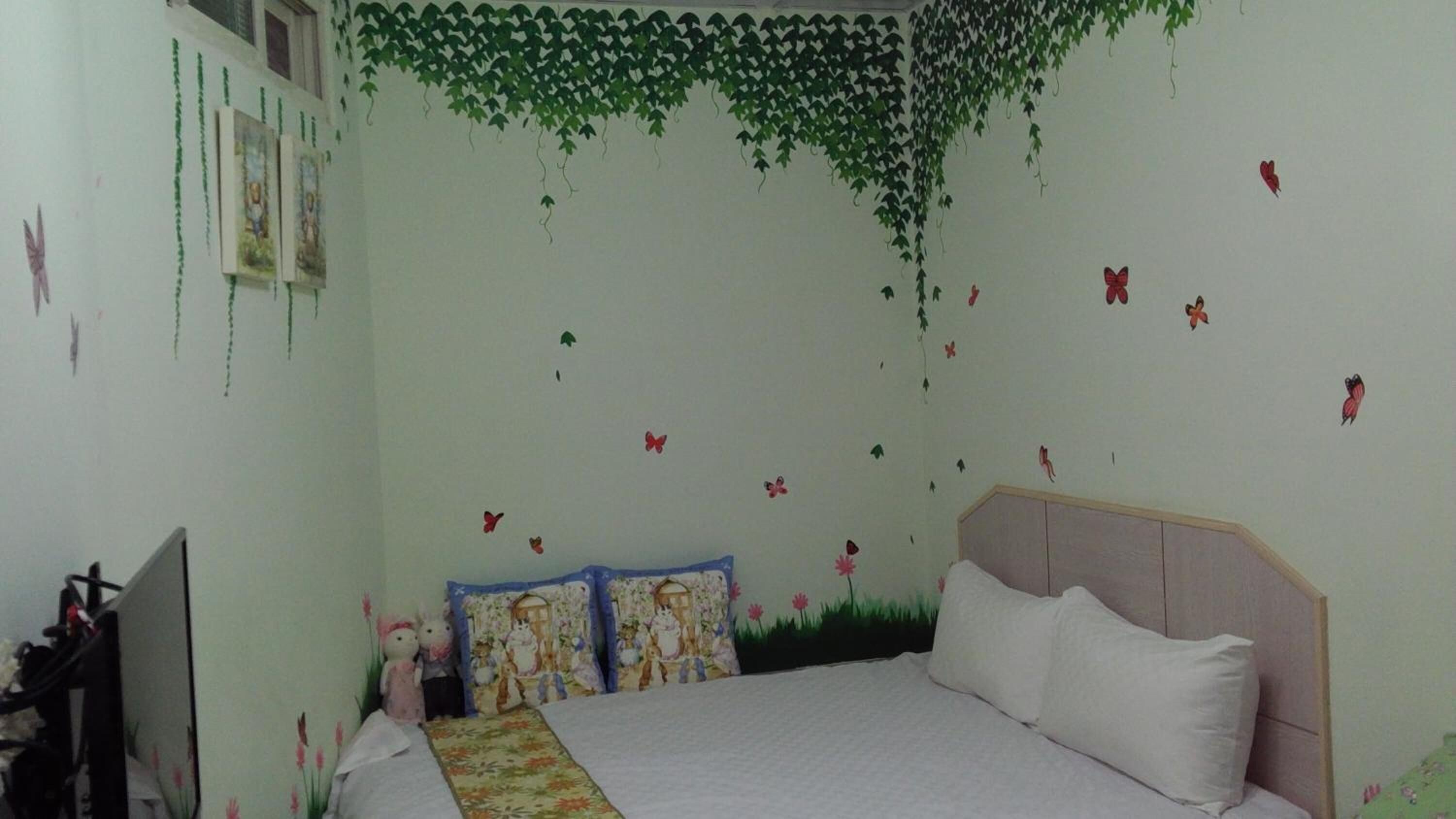 A bedroom with a bed, pillows, and a wall decorated with hanging vines and butterfly stickers.
