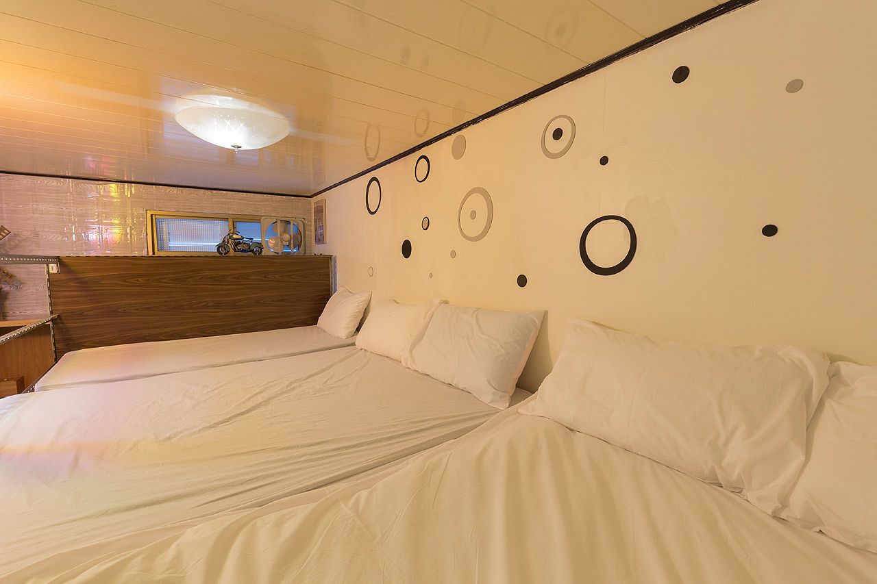 A hotel room with two beds, a wooden headboard, a large window, and a wall with circular patterns.