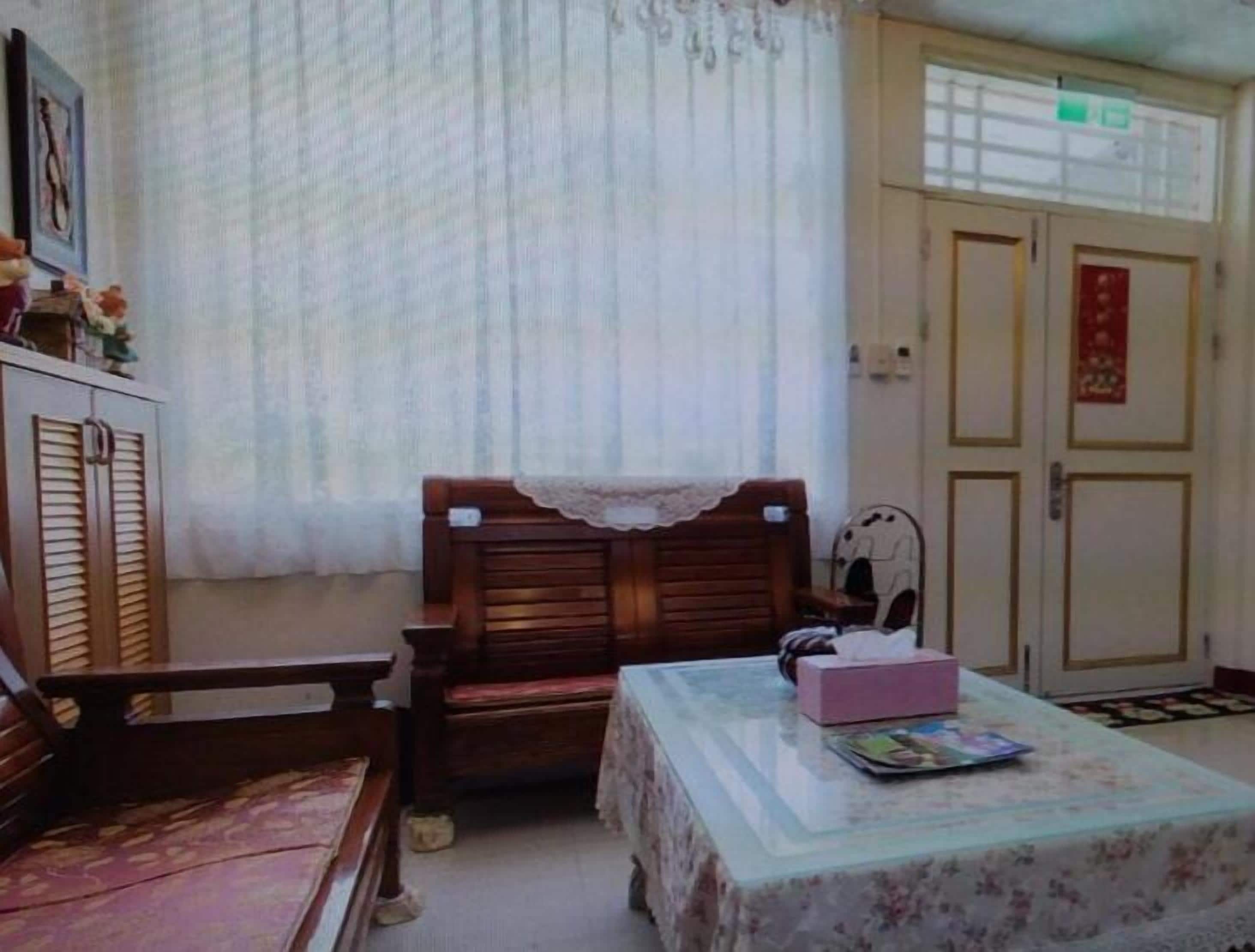 Una habitación pequeña con un banco de madera, una mesa con mantel floral y una puerta con un adorno rojo.
