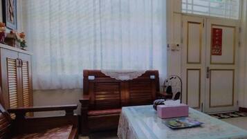 Una habitación pequeña con un banco de madera, una mesa con mantel floral y una puerta con un adorno rojo.