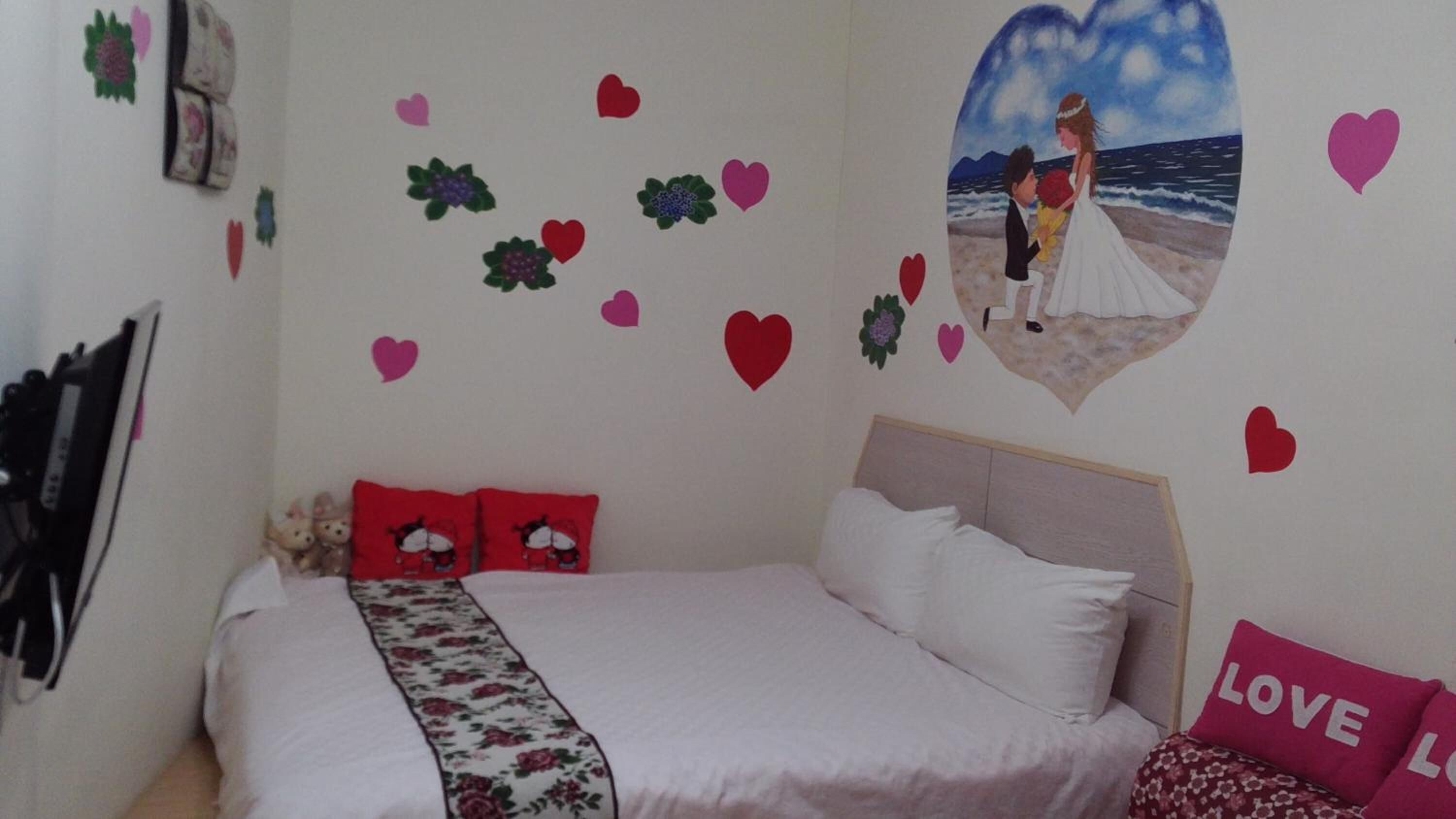 Un dormitorio con cama, almohadas, un adorno en forma de corazón y una estantería en la pared.