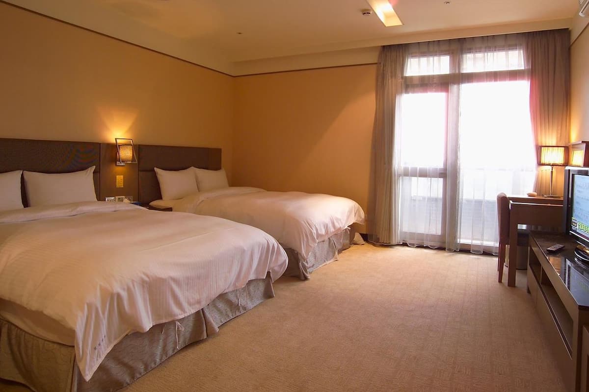 Quarto de hotel com duas camas, uma escrivaninha com televisão e uma janela com cortinas.