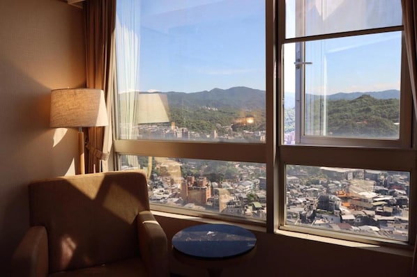 A hotel room with a large window offering a view of a cityscape and mountains.