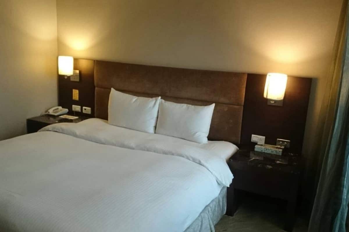 Quarto de hotel com cama grande, duas mesas de cabeceira, um criado-mudo e luminárias fixadas na parede.