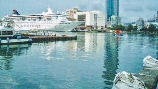 A waterfront scene with a cruise ship docked at a pier, a tall modern building, and a calm body of water reflecting the sky. - Rhineinn Hotel (Keelung)