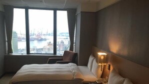 A hotel room with two beds, a chair, a nightstand, and a view of a cityscape through large windows. - Rhineinn Hotel (Keelung)
