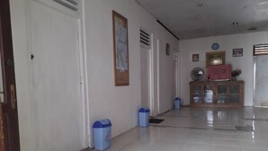 A hallway with white tiled floors, a wooden cabinet with glass doors, and a blue trash bin. - Harry & Mimin Homestay (Gorontalo)