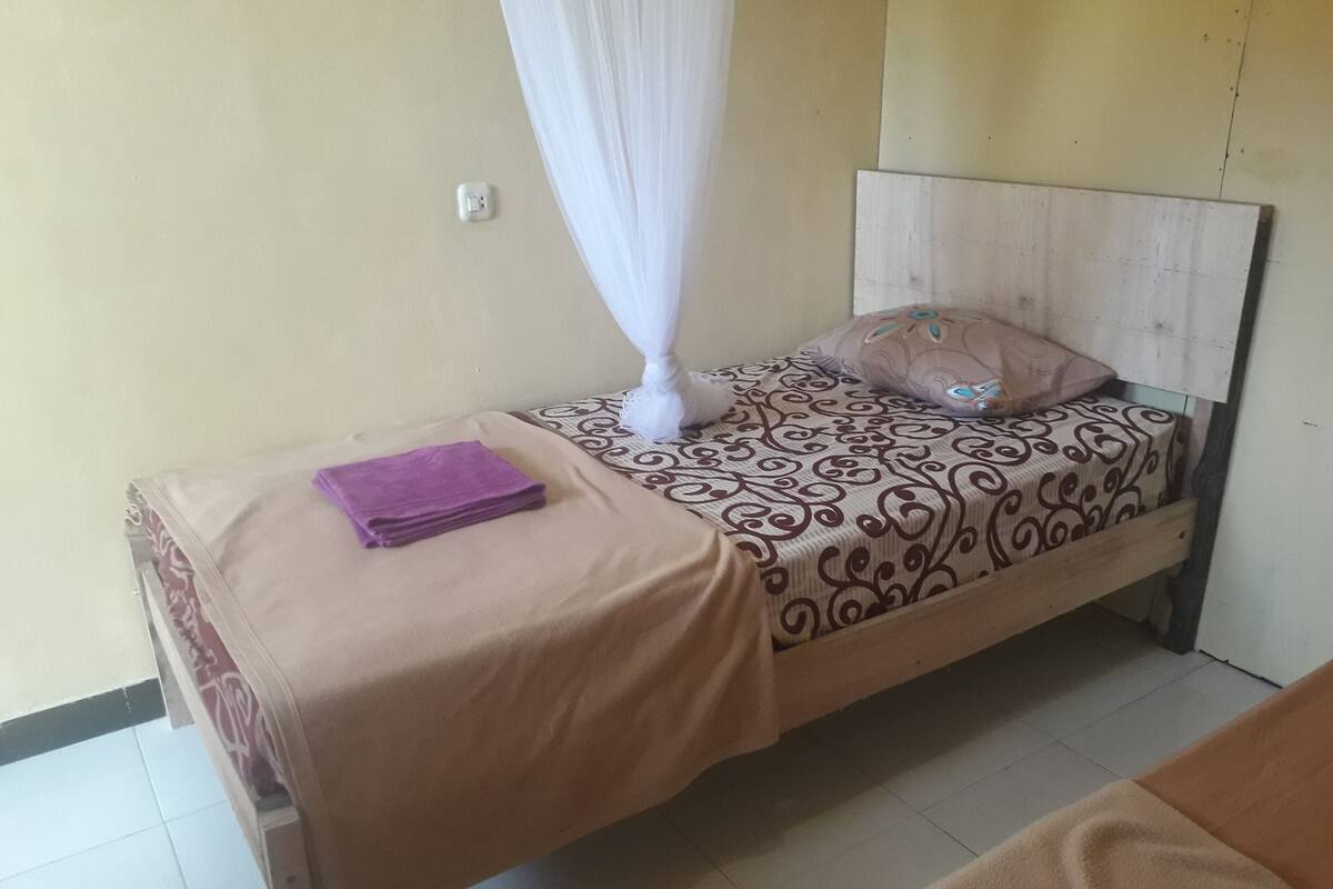 A single bed with a patterned bedspread, a white canopy, a purple towel, and a wooden headboard.