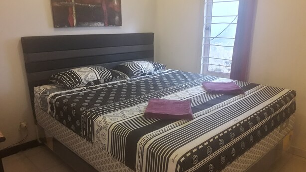 A neatly made bed with patterned bedding, a headboard, and a window with bars. - Harry & Mimin Homestay (Gorontalo)