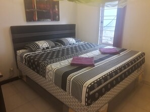 A neatly made bed with patterned bedding, a headboard, and a window with bars. - Harry & Mimin Homestay (Gorontalo)