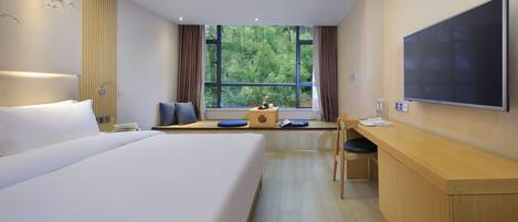 A hotel room with a large bed, a desk, a chair, a flat-screen TV, and a window with a view of trees.