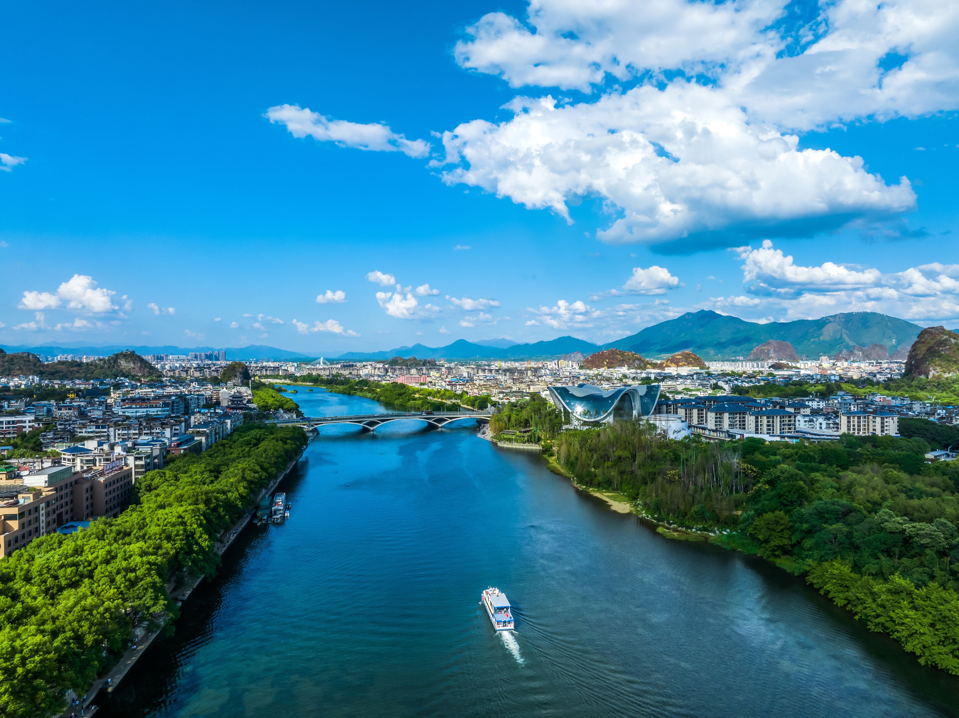 A river with a boat, surrounded by greenery and buildings.